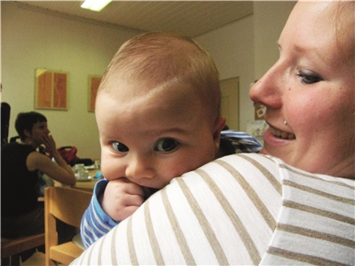 Das Foto zeigt eine Mutter mit einem Kleinkind auf dem Arm, das ihr über die Schulter schaut.