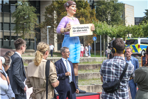 Dr. Frank Joh. Hensel steht vor der Figur 'Jenny' direkt vorm Düsseldorfer Landtag und begrüßt die Teilnehmenden der Caritas-Kundgebung