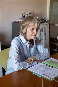 Porträt: Ulrike Langer in einer Beratungssituation. Auf dem Tisch steht eine Plexiglasscheibe, vor ihr liegt zudem eine aufgeschlagene Akte.