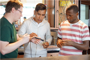 Ein Anleiter und zwei junge Flüchtlinge hantieren in einer Werkstatt an einem Werkstück herum