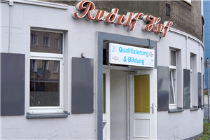 Der Eingang des Förderzentrums für junge Flüchtlinge in Hagen. Über der Tür hängt der Name der ehemaligen Eckkneipe 'Rudolf Huf' und das Schild 'Qualifizierung und Bildung'.