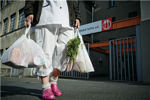 Eine Kundin steht vor einer Ausgabenstelle der Arnsberger Tafel e. V. und trägt zwei gefüllte Plastiktüten