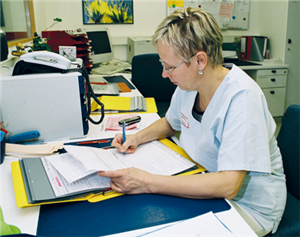 Eine weibliche Leitungskraft in einem Krankenhaus sitzt an ihrem Arbeitsplatz und bearbeitet eine Akte