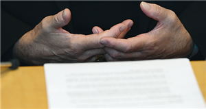 Die miteinander verbundenen Hände von Bischof Dr. Felix Genn, die an einem Tisch lehnen. Davor liegt ein Blatt Papier.