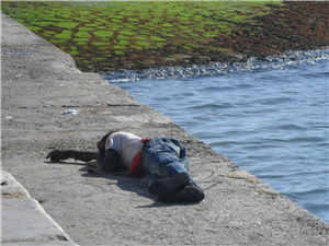 Ein Obdachloser, der auf einem Steinboden am Ufer des Tejo in Lissabon liegt