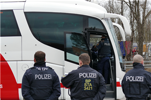 Drei Bundespolizisten, die mit dem Rücken zur Kamera gewandt, vor einem weiß-roten Reisbus stehen. Durch die geöffnete Tür ist der Fahrer und ein weiterer Polizist zu sehen.