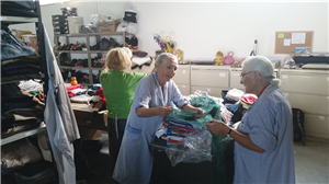 Drei ehrenamtliche tätige Frauen sortieren in einer Kleiderkammer an einer Theke gespendete Kleidung.