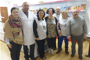 Eine Gruppe von sieben Freiwilligen, die in einem Sozial-Supermarkt der Caritas in León (Spanien) vor einer Regalwand und zwei Kühltruhen stehen