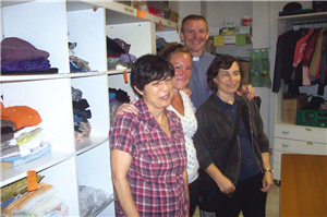 Drei Mitarbeiterinnen einer Kleiderkammer und der Pfarrer der Gemeinde S. Giuseppe Cafasso in Turin stehen vor einem Kleiderregal