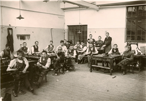 Historische Aufnahme in Schwarz-Weiß: Eine Gruppe von Männern mit Behinderung sitzen in der Schumacherwerkstatt des Josefsheims in Bigge an Werkbänken und stellen Schuhe her