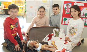 Zwei Schülerinnen und zwei Schüler knien in einem Raum einer offenen Ganztagsschule der Caritas Gelsenkirchen vor einem geöffneten Koffer. Darin ist eine Puppen und eine weiße Decke zu sehen.