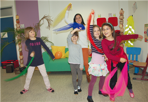 Yanine Itzu Perdomo Rivera und vier Schülerinnen einer OGGS in Soest stehen in einem bunt möbilierten Raum und spielen mit farbigen Tüchern