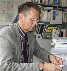 Andreas Sellner sitzt in seinem Büro an seinem vollgepackten Schreibtisch und blickt auf einen Zettel, den er in den Händen hält