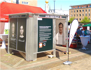 Ein Kubus der Caritas- Aktion 'Stell mich an, nicht aus' aus Metall mit einigen Plakaten, der auf einem Platz in Dortmund steht