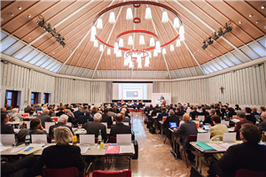 Die Teilnehmer der Caritas-Delegiertenversammlung vom 12.10.2016 in Köln, die an langen Tischreihen sitzen und auf die Bühne blicken. An der Decke ist ein großer Leuchter zu sehen.