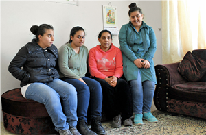 Noelle Tannous sitzt mit ihren drei Töchtern in einem karg eingerichten Wohnraum auf einem braunen Sofa