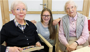 Zwei ältere Frauen sitzen in einem Gemeinschaftsraum des Pauline-von-Mallinckrodt-Hauses in Paderborn auf Stühlen, eine junge Frau hockt dazwischen