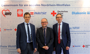 Gruppenfoto mit Dr. Frank Joh. Hensel, Andreas Johnsen und Hermann Zaum vor einer Stellwand der LAG Freie Wohlfahrtspflege NRW