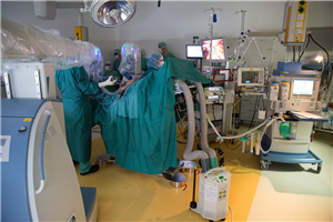 Ein Operationssaal in dem einige Mediziner mit OP-Robotern eine Operation durchführen. Neben dem Operationstisch sind auch einige Geräte und Anschlüsse zu sehen.