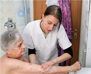 Eine Altenpflegerin steht in einem Badezimmer und wäscht den Arm einer Seniorin