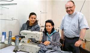 Domkapitular Dr. Thomas Witt steht neben zwei Frauen die an einer Nähmaschine arbeiten