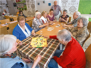 Eine Gruppe von Senior/innen sitzt mit einer Beraterin an einem Tisch im Café des 'zentrum plus' und spielen Karten- und Gesellschaftsspiele
