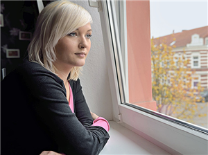 Eine junge Frau leht auf einer Fensterbank und blickt nachdenklich aus einem Fenster