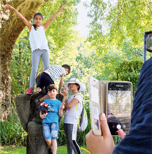 Ein Mädchen steht auf einer Statue in der Essener Gruga und streckt die Arme in die Luft. Ein weiteres Kind klettert auf die Statue, zwei weitere Kinder und eine Frau mit Handy stehen davor.