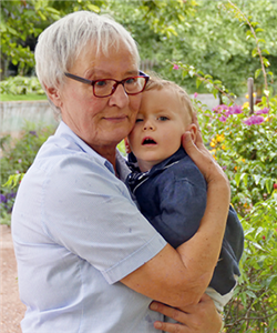 Porträt: Saskia von der Heyden, die mit einem Kind im Arm in einem Garten steht