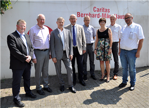 Vertreter/innen der Caritas in NRW und des MAGS NRW, die in Dortmund vor einer Mauer mit dem Schriftzug "Caritas Bernhard-März-Haus" stehen