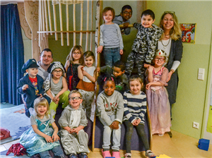 Gruppenfoto mit einer Betreuerin, einem Betreuer und 13 Kindern in einem Spielzimmer einer Kindertageseinrichtung