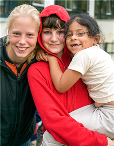 Drei Mädchen halten die Köpfe zusammen und lächeln in die Kamera. Ein Mädchen trägt ein anderes, kleineres Mädchen auf dem Arm.