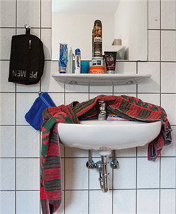 Ein Waschbecken mit Ablage und Spiegel in eine Waschraum. Die Ablage ist mit Hygieneartikel vollgestellt, quer über dem Waschbecken liegt ein Handtuch.