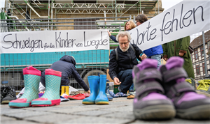Eine Schweigeaktion in Hameln, bei der drei Frauen und ein Mann ein Banner zum Missbrauchsskandal von Luegde an einem Bauzaun befestigten und viele Kinderschuhe auf den Boden stellten