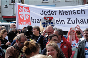 Demonstranten auf einer Demonstration an einem Aktionstag des NRW-Bündnisses 'Wir wollen wohnen!' am 6. April 2019 in Köln. Im Hintergrund ist ein großes Banner der Caritas zu sehen. 