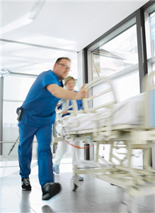 Eine Krankenpflegerin und ein Krankenpfleger schieben ein Krankenbett über den Gang eines Krankenhauses