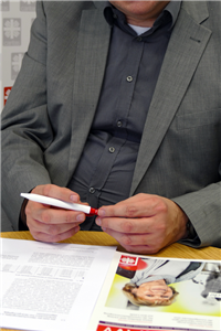 Porträt: Roman Schlag, der an einem Tisch sitzt und einen Stift in seinen Händen hält. Vor ihm liegt eine Ausgabe der Zeitschrift 'Caritas in NRW' und einige Notizen.