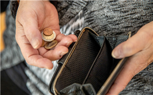Eine Seniorin, die Kleingeld und eine leere Geldbörse in den Händen hält. Der Foto ist auf die Hände der Seniorin fokussiert.