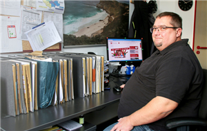 Stefan Beckmann an seinem Arbeitsplatz sitzt an seinem Arbeitsplatz. Auf dem Schreibtisch steht eine große Zahl von Akten.