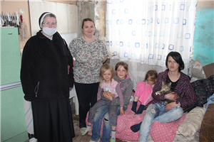 Schwester Alberta steht zusammen mit einer bedürftigen Familie in einem heruntergekommen Wohnraum, der sich in einem Haus in Mamonowo befindet.