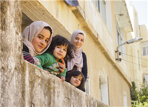 Eine Frau und drei Kinder gucken lächelnd von einem Balkon in Jordanien in die Kamera