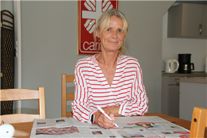 Porträt: Sabine Walczak, die an einem Holztisch vor einigen Unterlagen sitzt. Im Hintergrund ist ein Caritas-Logo an der Wand zu sehen.