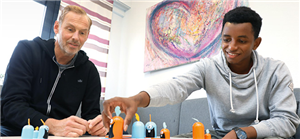 Ein Geflüchteter sitzt mit dem Bereichsleiter eines Jugendhauses in Mönchengladbach zusammen und spielt mit ihm ein Gesellschaftsspiel