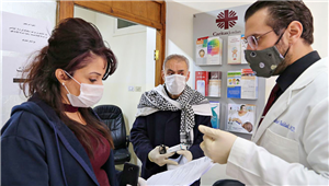 Ein Arzt spricht in den Räumlichkeiten der Caritas Jordanien mit einer Frau und einem Senior. Alle tragen Einweghandschuhe und Schutzmasken.