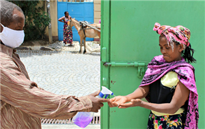 Ein Caritas-Mitarbeiter steht mit einer Frau vor einem grünen Container und sprüht ihre Hände mit Desinfektionsmittel ein
