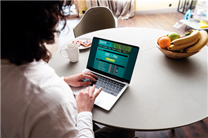 Eine Frau sitzt an einem Esstisch vor einem Laptop und surft auf einer Website für Sportwetten