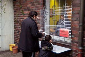 Ein Bewohner des Wilhelm-Sternemann-Hauses mit Kind, der mit einer Mitarbeiterin durch ein mit Folie gesichertes Fenster redet