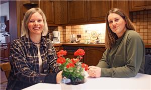Jessica Tepass und Pia Schuyesmans sitzen in einer Wohnküche an einem Tisch und blicken in die Kamera