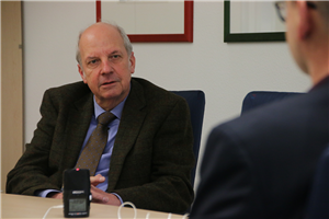 Heinz-Josef Kessmann sitzt an einem Besprechungstisch vor einem Tischmikrofon und blickt in Richtung des Interviewers Markus Lahrmann