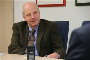 Heinz-Josef Kessmann sitzt an einem Besprechungstisch vor einem Tischmikrofon und blickt in Richtung des Interviewers Markus Lahrmann